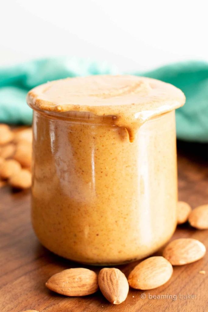 overflowing jar of almond nut butter with almonds surrounding it